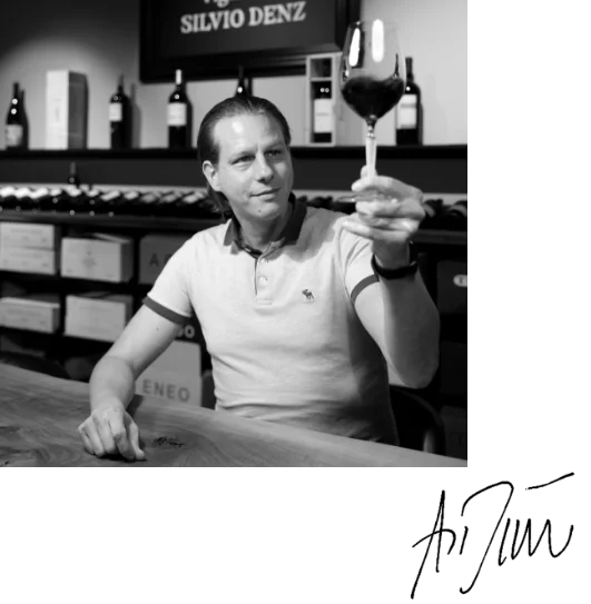 Geschäftsführer Denz Auktionen Andreas Dünner am Tisch hebt ein Glas Rotwein - Vinothek Denz Weine Zürich - mit Signatur