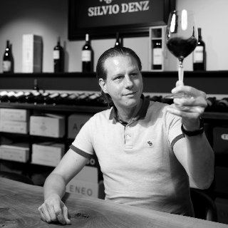 Geschäftsführer Denz Auktionen Andreas Dünner am Tisch hebt ein Glas Rotwein - Vinothek Denz Weine Zürich