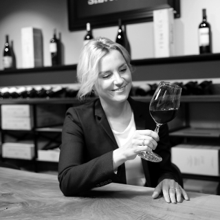 Weinkennerin und Geschäftsführerin Florentina Denz am Tisch mit einem Glas Rotwein - Vinothek Denz Weine Zürich