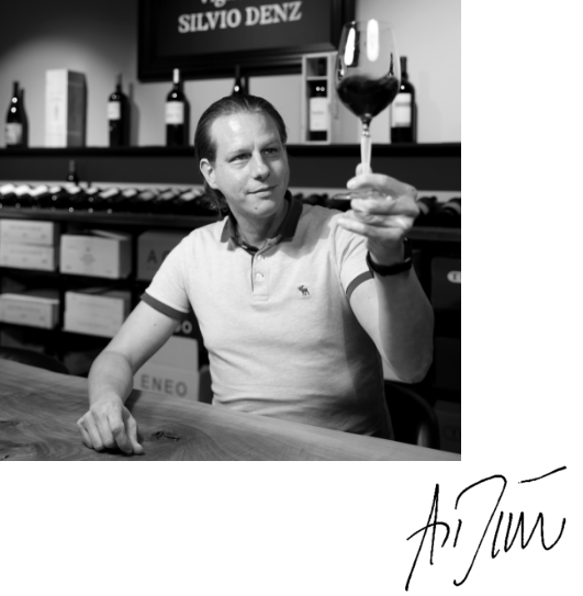 Geschäftsführer Denz Auktionen Andreas Dünner am Tisch hebt ein Glas Rotwein - Vinothek Denz Weine Zürich - mit Signatur